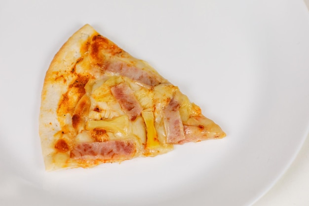 Closeup studio shot of one piece of tasty delicious Italian homemade mozzarella cheesy ham and pineapple original Hawaiian pizza soft bread crust on white dish plate served on table in restaurant