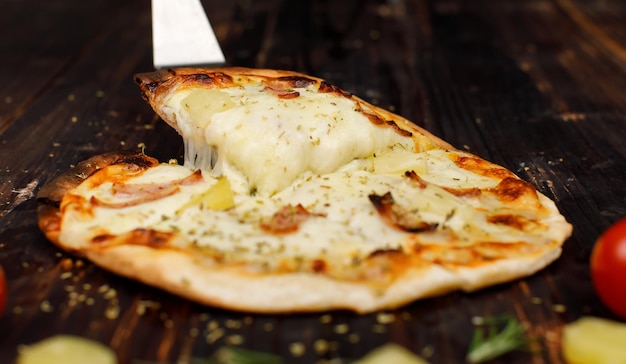 Closeup studio shot unrecognizable chef using stainless scoop peel picking up stretching cheese hot oven baked tasty delicious Italian homemade ham pineapple traditional Hawaiian bread crust pizza