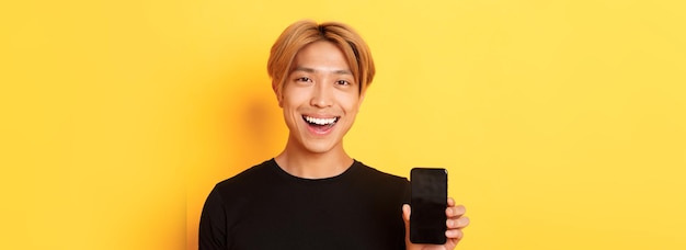 スタイリッシュなハンサムな韓国人のクローズ アップ スマート フォンの画面を表示し、笑顔を喜んで携帯電話をお勧めします