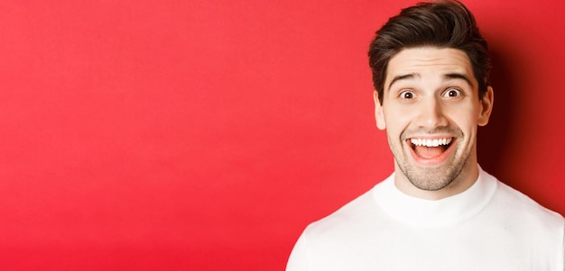 Closeup of surprised happy guy in white sweater looking amused hear interesting news standing over r...