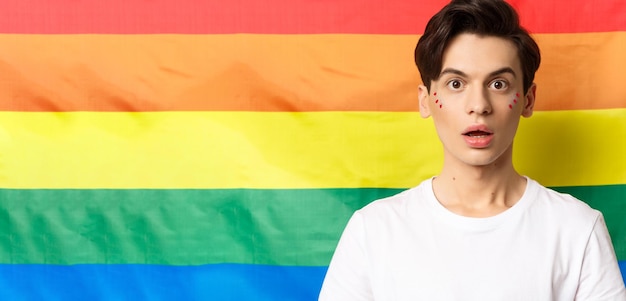 Closeup of surprised queer person with glitter on face looking amazed at camera standing over lgbtq