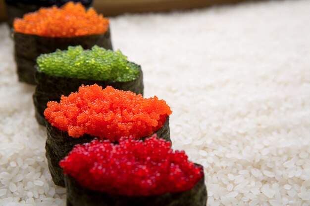 Closeup of sushi gunkan with colored caviar on white rice background and texture copy space