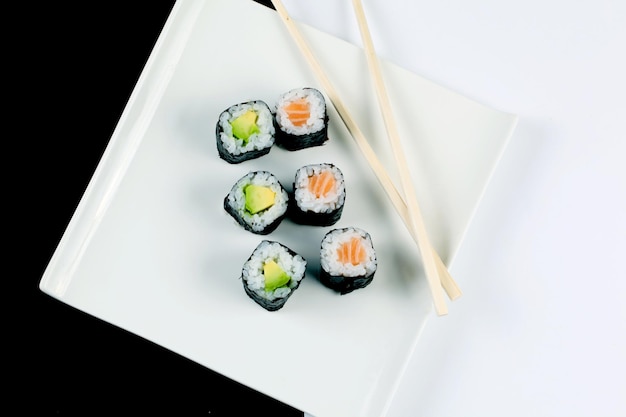 Closeup of sushi rolls on a white plate with wooden sticks