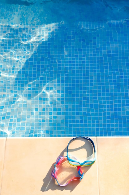 Closeup of swimming goggles on the edge of the summer pool