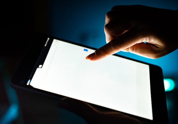 Foto primo piano del tablet con schermo bianco e mano degli utenti su sfondo scuro