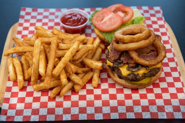 Крупный план вкусных гамбургеров с говядиной или сыром и луковым кольцом с картофелем фри и кетчупом на черном столе на черном фоне