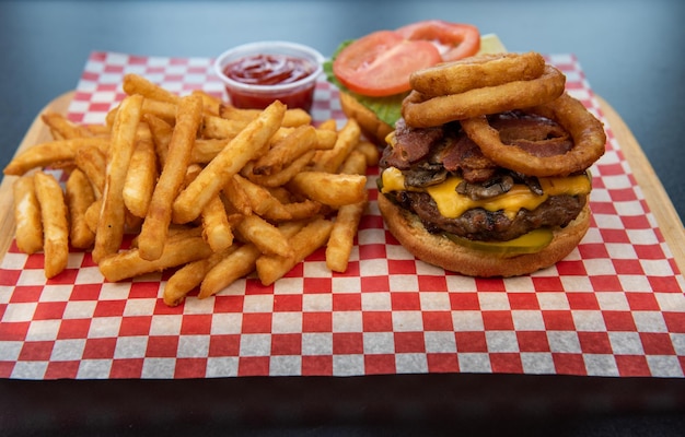 Closeup of tasty hamburgers with beef meat or cheese and onion ring with french fries and ketchup on a black table against black background