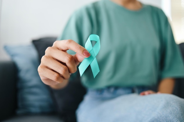 Photo closeup teal awareness ribbon holded by woman hands to support cancer survivor