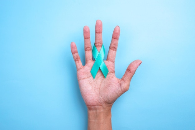 Photo closeup teal awareness ribbon on woman hands to support cancer survivor