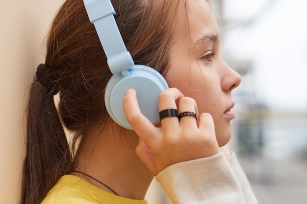 Closeup of a teenage girl in a sweater listening to music uses wireless headphones outdoors