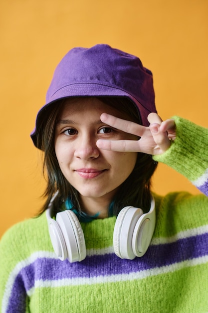 Closeup of teenager in headphones and hat posing at camera isolated on orange background