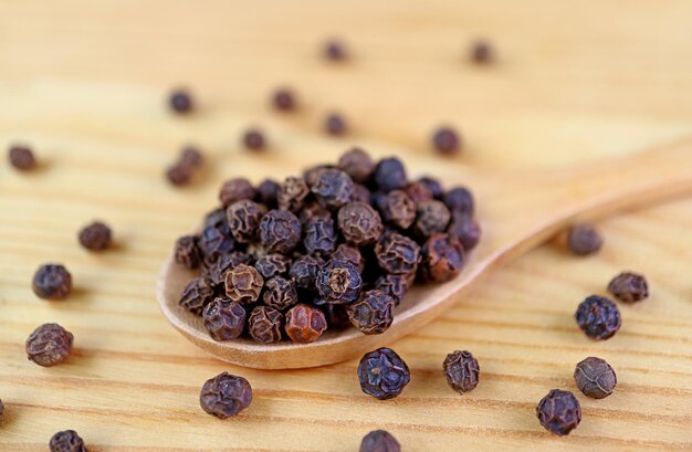 Closeup the texture of black peppercorns on wooden spoon with some scattered around