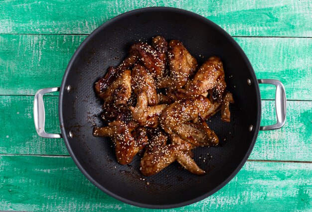 Photo closeup of a thai recipe with caramelized chicken wings in a wok pan on green wooden table