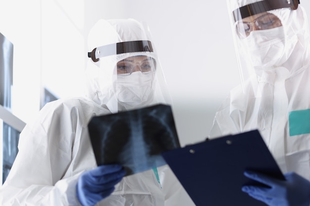 Closeup of therapists in protective medical suits looking carefully at radiograph of sick patient