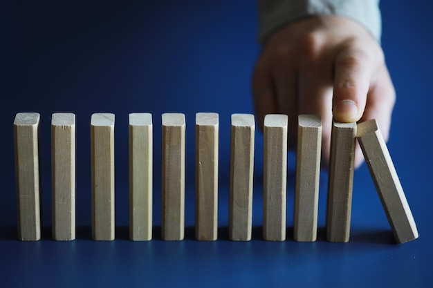 Il blocco di legno di domino spesso del primo piano in una fila ferma la caduta essere stabile nel concetto di soluzione di affari di crisi