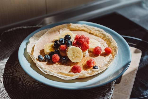 Closeup of thin pancakes with berries and bananas in a plate on the table