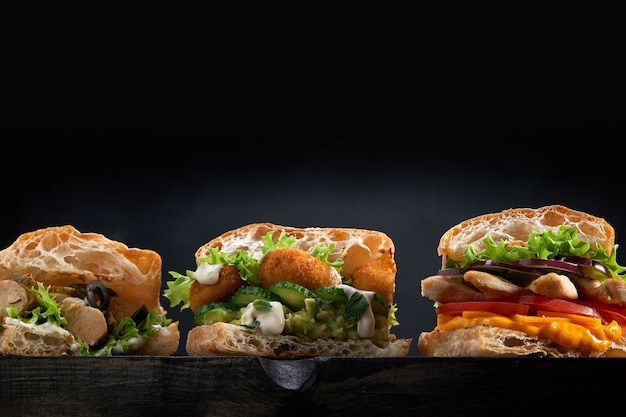 Closeup of three different Appetizing sandwiches burgers on black wooden background