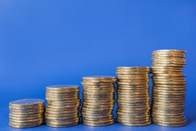 Closeup of three stack of gold coins on blue background.