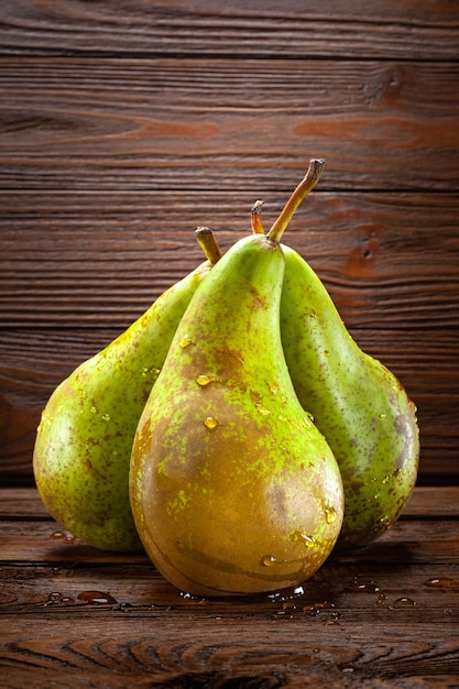 Closeup of three wet pears with drops of water on a dark wooden background Vertical composition