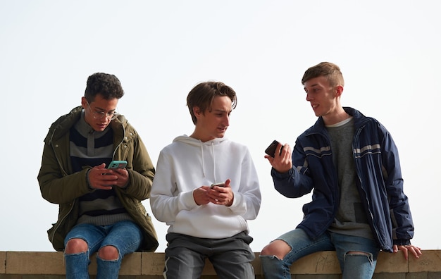 A closeup of three young Caucasian and Hispanic guys socializing and using their smartphones