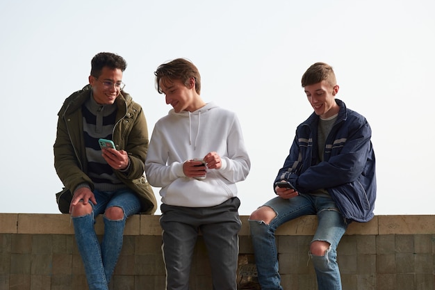 A closeup of three young Caucasian and Hispanic guys socializing and using their smartphones