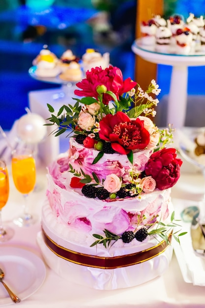 A closeup of a tiered cake decorated with red peonies roses an