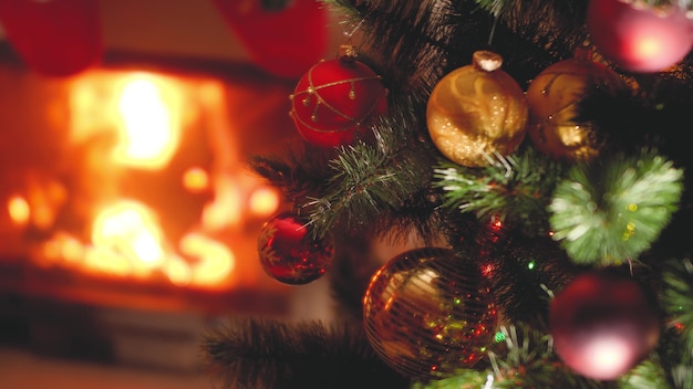 Closeup toned footage of Christmas tree branches with baubles and lights against burning firepalce