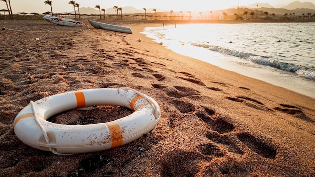 Closeup toned image of life saving ring lying on the sea baech sand. Beutiful sunset over the ocean