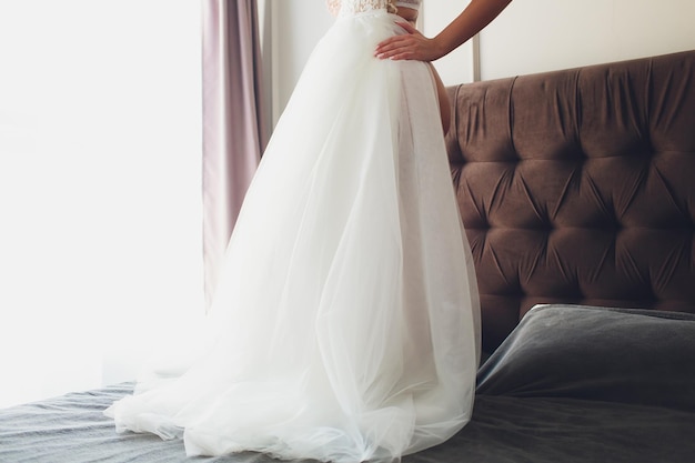 Closeup toned photo of beautiful bride tying up her wedding dress