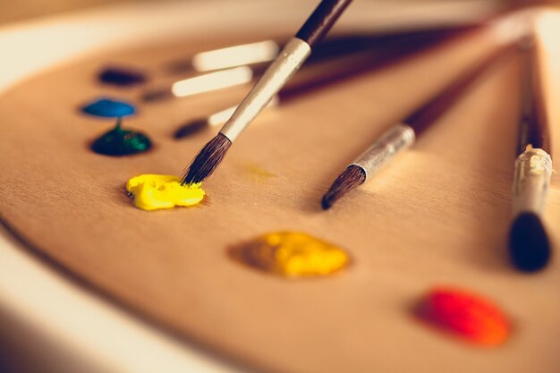 Closeup toned photo of paintbrushes lying on palette dipped in oil paints