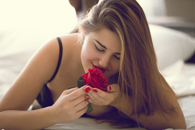 Closeup toned portrait of sexy woman posing with red rose in bed