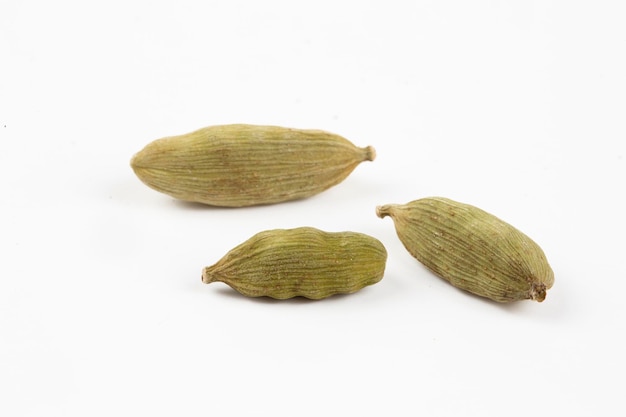 흰색 배경에 흩어져 있는 씨앗, 카다멈 향신료가 있는 말린 녹색 엘레타리아 카다모뭄 과일의 클로즈업 상단 보기