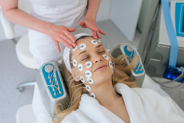 Closeup top view of hardware electro myostimulation procedure at beauty spa salon cosmetologist apply equipment on patient relaxed face