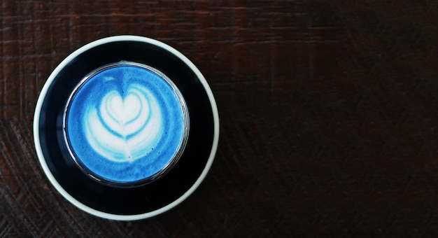 Photo closeup top view of hot butterfly pea latte on dark wooden table