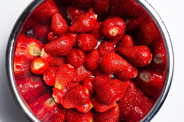 Closeup top view of steel bowl with strawberries on white background