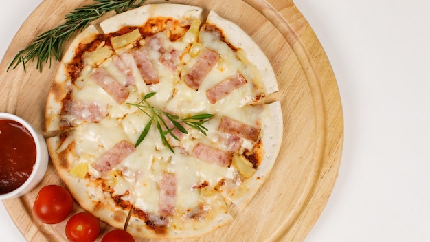 Closeup top view studio shot of round hot oven baked tasty delicious Italian homemade ham pineapple original Hawaiian soft bread crust pizza on wooden plate pan with tomatoes and ketchup on table