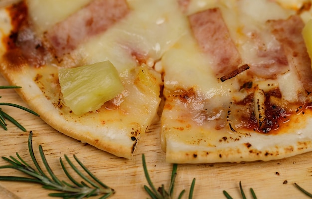 Closeup top view studio shot of round hot oven baked tasty delicious Italian homemade ham pineapple original Hawaiian soft bread crust pizza on wooden plate pan with tomatoes and ketchup on table