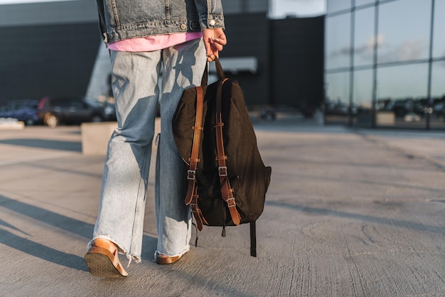 Foto primo piano dello zaino turistico da donna vista posteriore di una giovane donna vestita di jeans e con borsa nera che cammina per strada in città