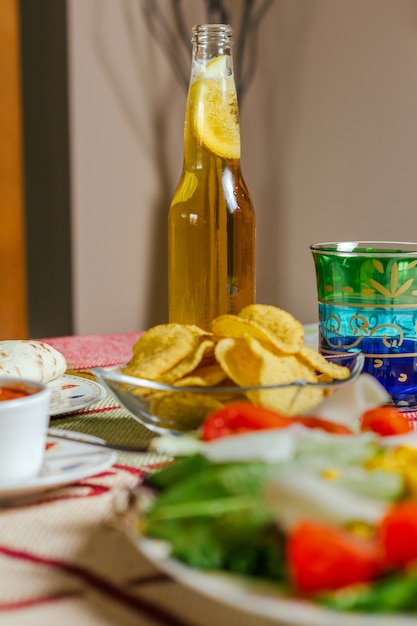 Closeup of traditional mexican food in a table, with a bowl of nachos, spicy sauce, a plate of salad and a fresh beer. Selective focus on beer bottle in background