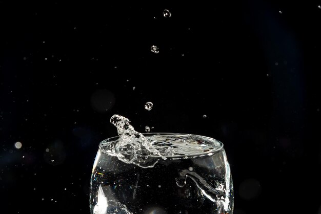 Foto close-up di una tazza di vetro trasparente con acqua all'interno e gocce che fanno uno spruzzo