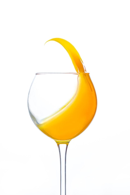 白い背景にオレンジジュースがはねている透明なワイングラスのクローズアップ