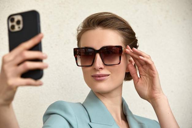 Closeup of trendy girl face in sunglasses is making selfie photo