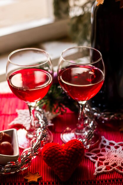 Foto primo piano due bicchieri di vino rosso sul tavolo di capodanno decorato festivo sullo sfondo della finestra chiara