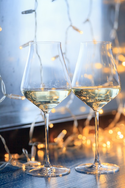 Closeup of two glasses of white wine in transparent crystal glasses and light garlands