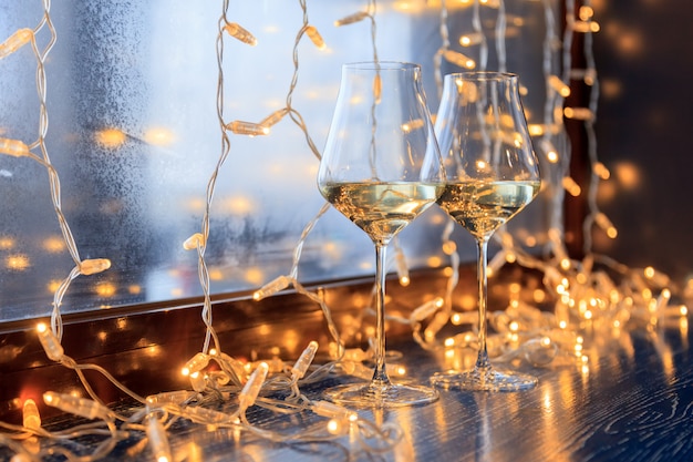 Closeup of two glasses of white wine in transparent crystal glasses and light garlands