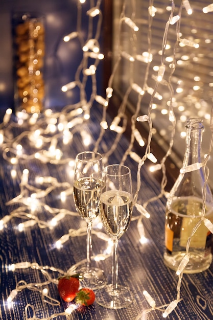 Closeup of two glasses of white wine in transparent crystal glasses, strawberries, reserved signs and light garlands