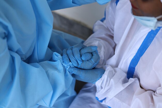 Closeup of two Indian healthcare workers in protective clothing, holding hands for support