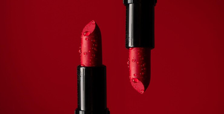 Closeup on two red lipsticks in splashes of water on a red background