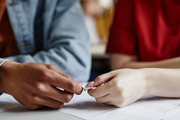 Closeup of two students passing note in secret gossiping or\
cheating on test copy space