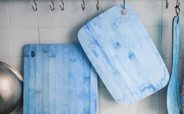 Closeup of two wooden cutting boards hanging on a tiled wall on metal hooks blue tinted